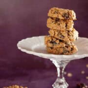 Close-up of 5 stacked oatmeal raisin cookies on a glass pedestal plate.