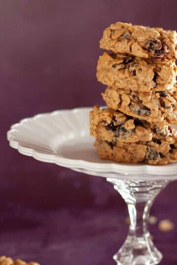 Close-up of 5 stacked oatmeal raisin cookies on a glass pedestal plate.