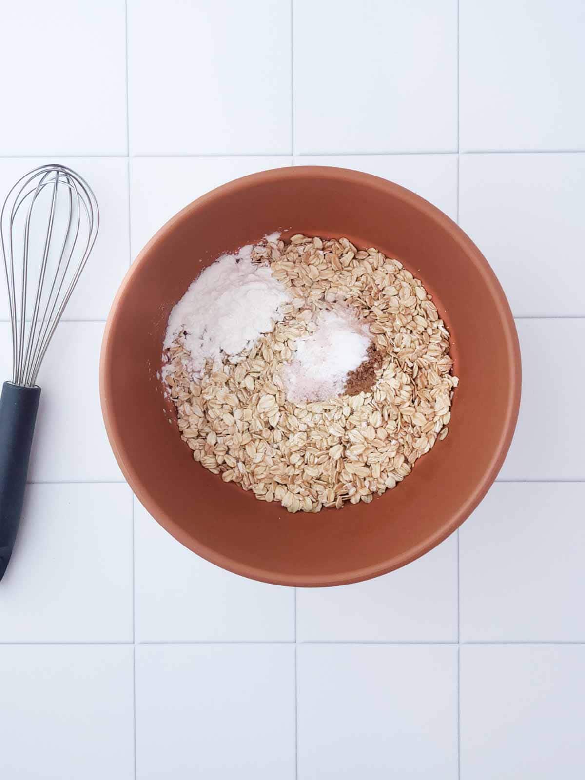 Rolled oats with baking powder, soda, cornstarch, cinnamon, and salt in mixing bowl.