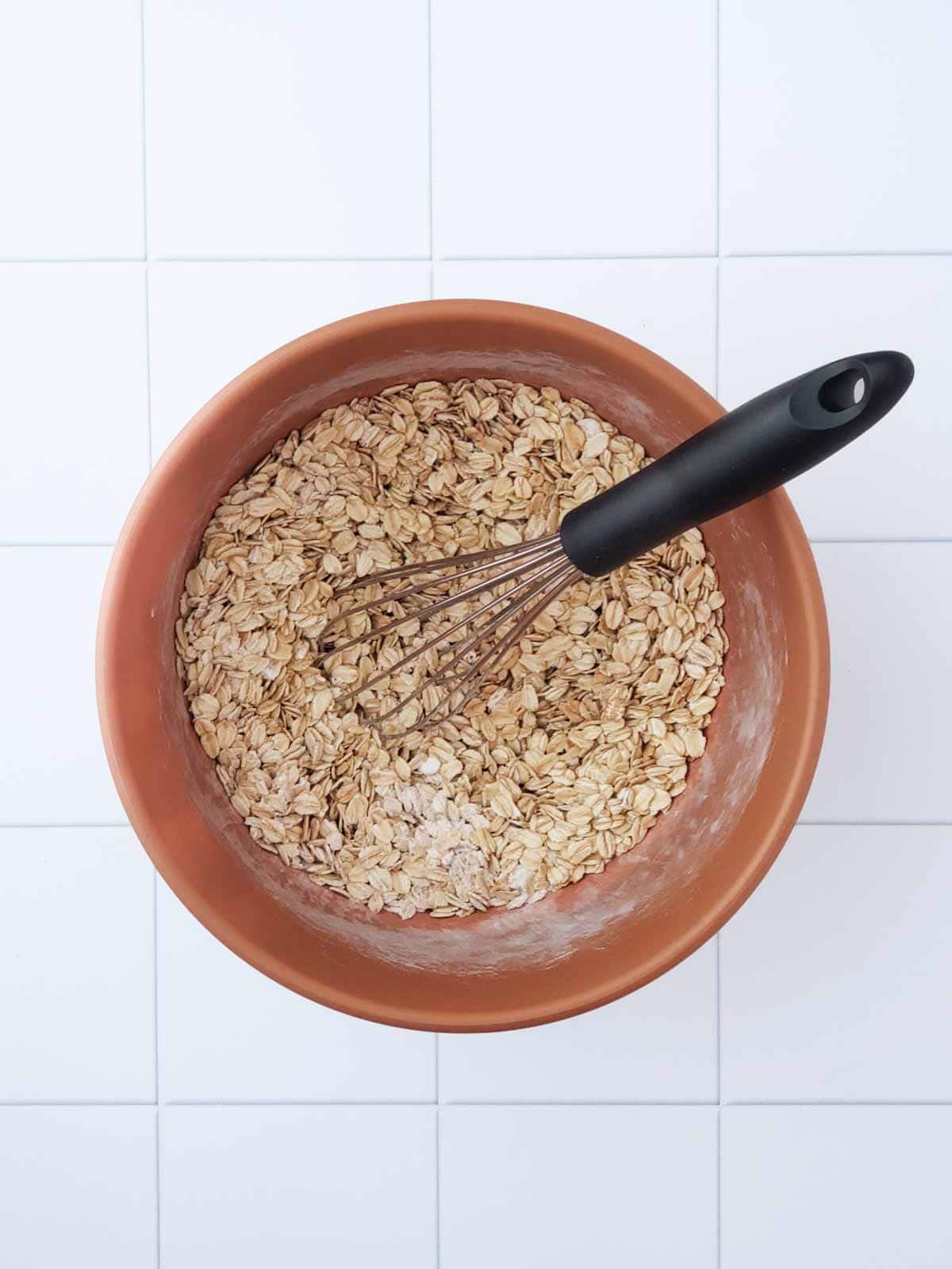 Mixing bowl with rolled oats and whisk for oatmeal raisin cookies.