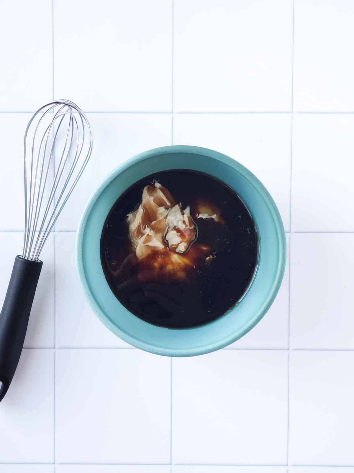 Mixing bowl with cashew butter, maple syrup, and molasses before mixing, with whisk on the side.