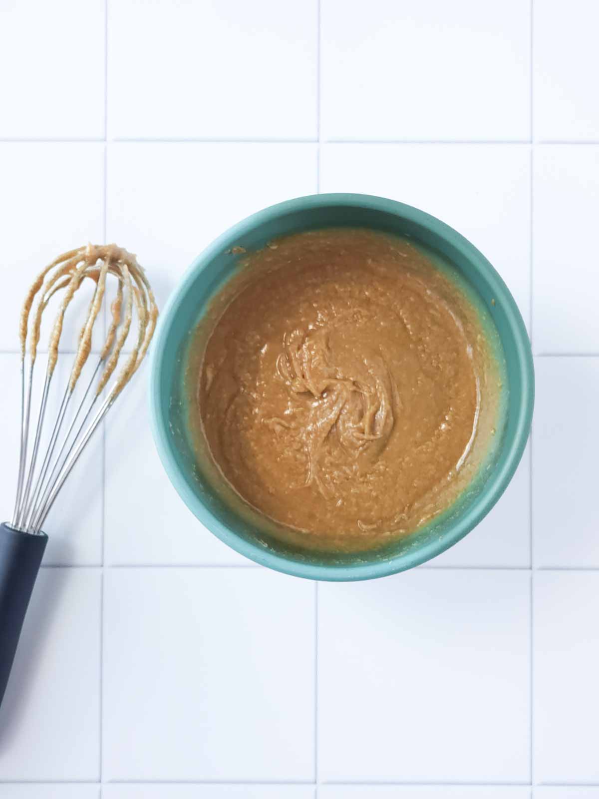 Green bowl with whisk and creamy cashew cookie wet ingredient batter.