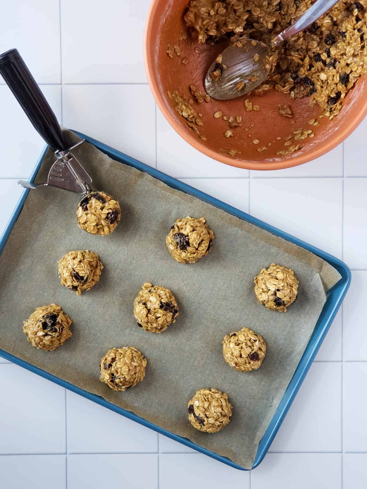 Scoops of oatmeal raisin cookie dough on a parchment-lined baking sheet.
