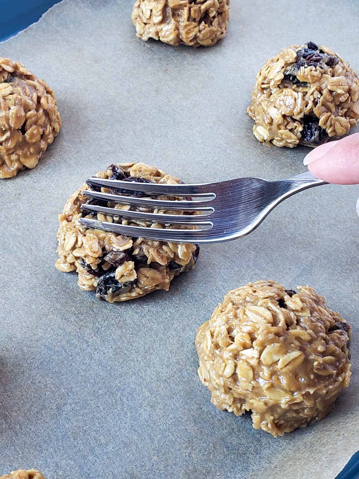 A hand holding a fork on a cookie demonstrating how to gently press before baking.