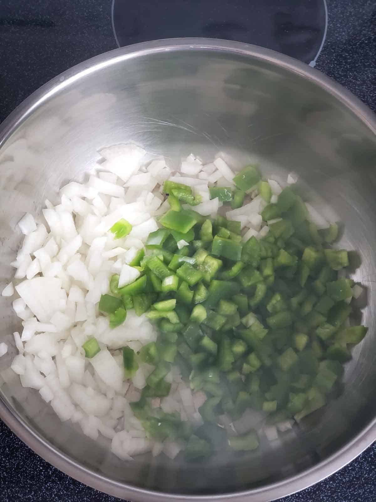 Chopped onion and green bell pepper cooking in a pot.