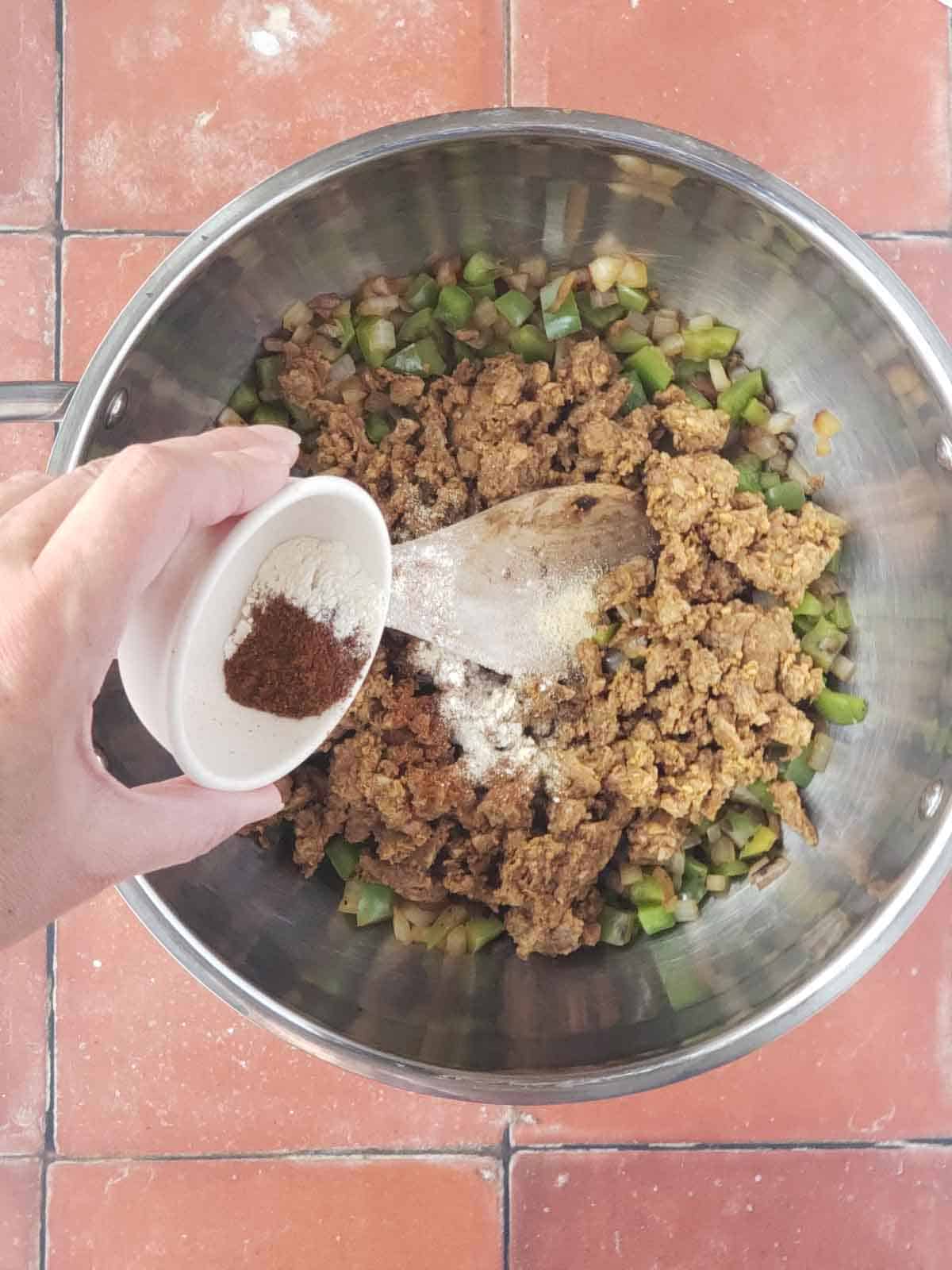 Hand adding spices to plant-based grounds and vegetables.