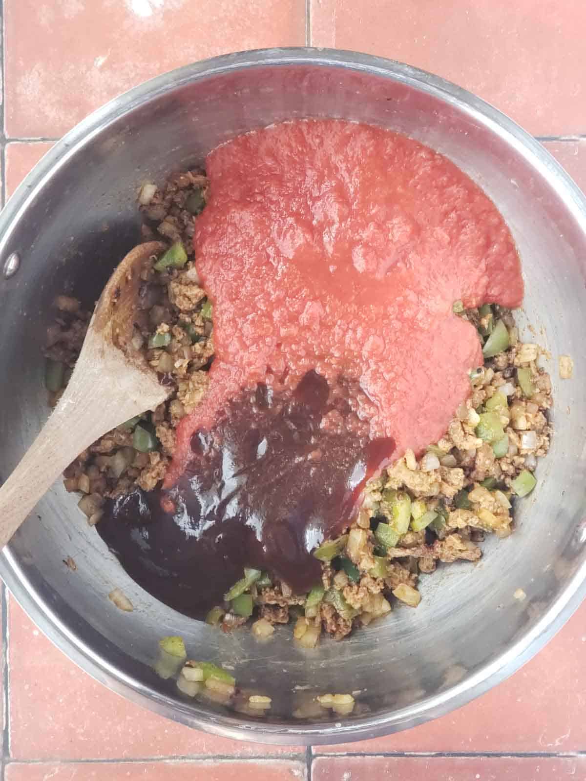 Crushed tomatoes and BBQ sauce poured into pot with vegan meat and veggies.
