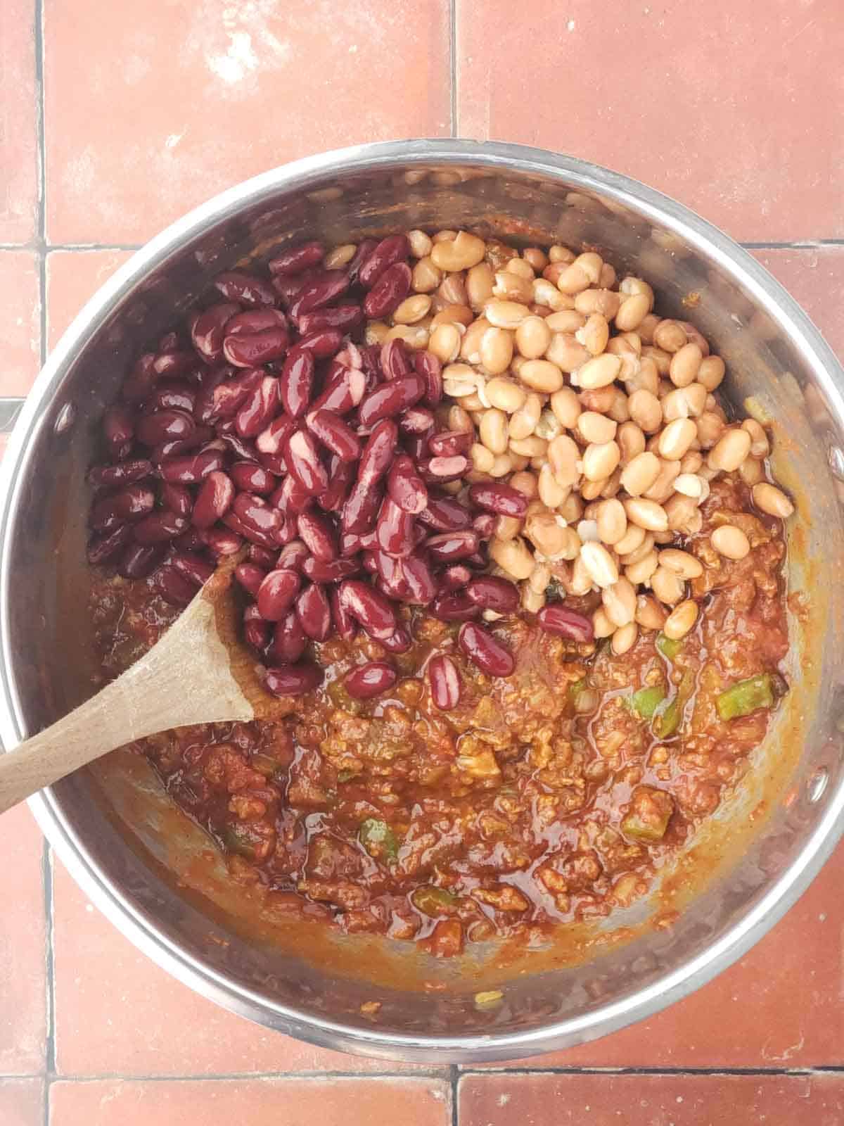 Kidney beans and pinto beans added to pot of simmering vegan chili with vegetables and plant-based ground.