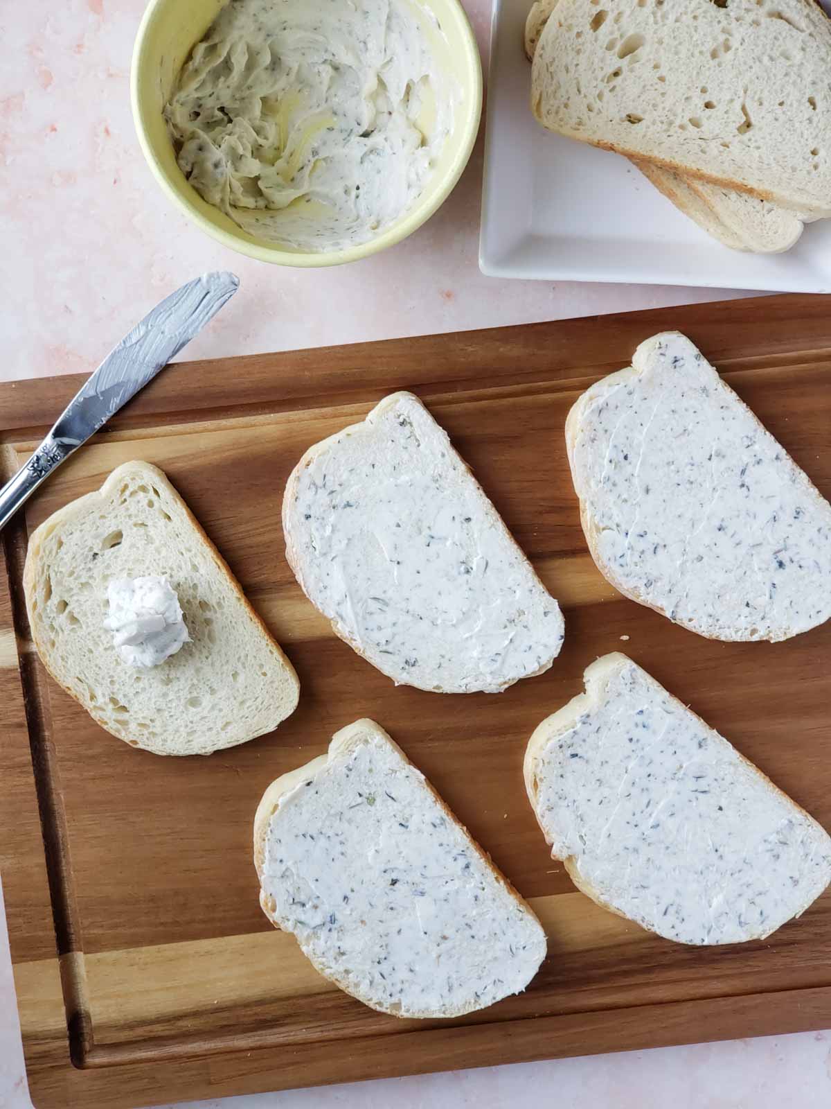 Cutting board with sourdough slices coated in seasoned butter spread, ready for toppings.