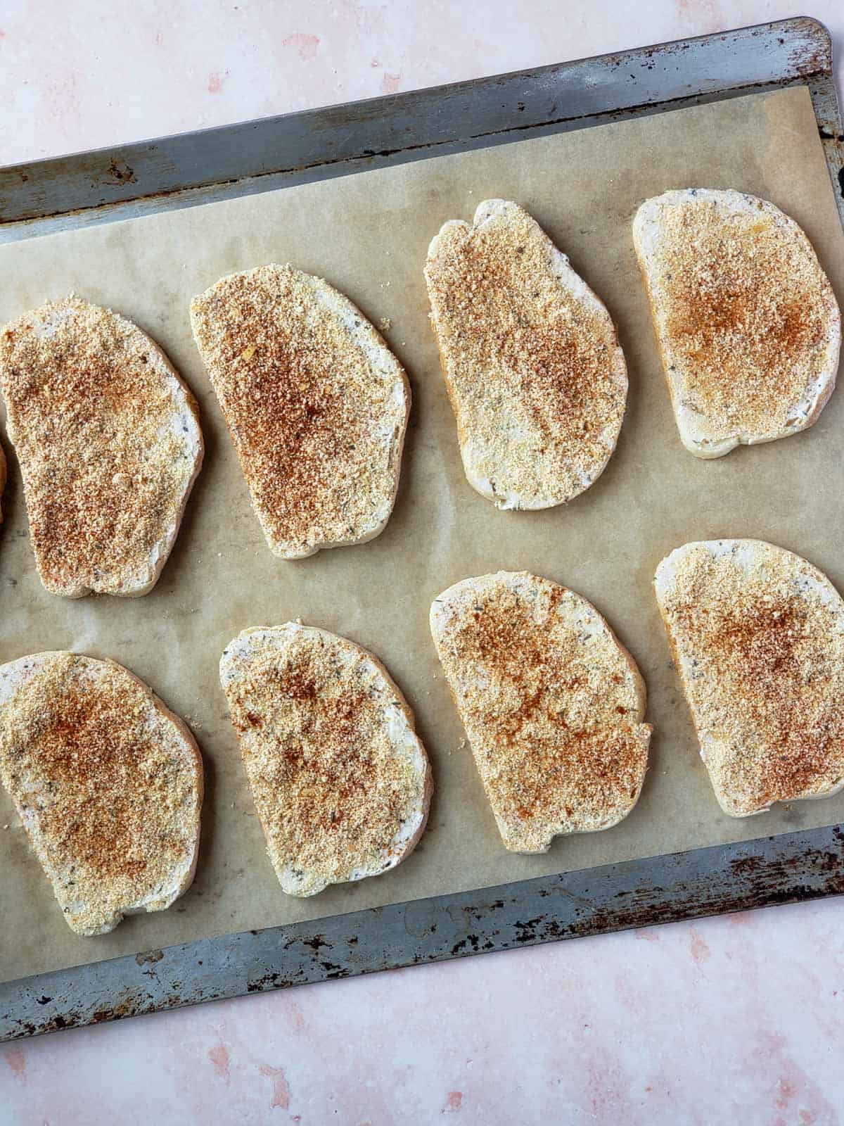 Overhead view of eight seasoned sourdough slices on a parchment lined tray ready for baking.