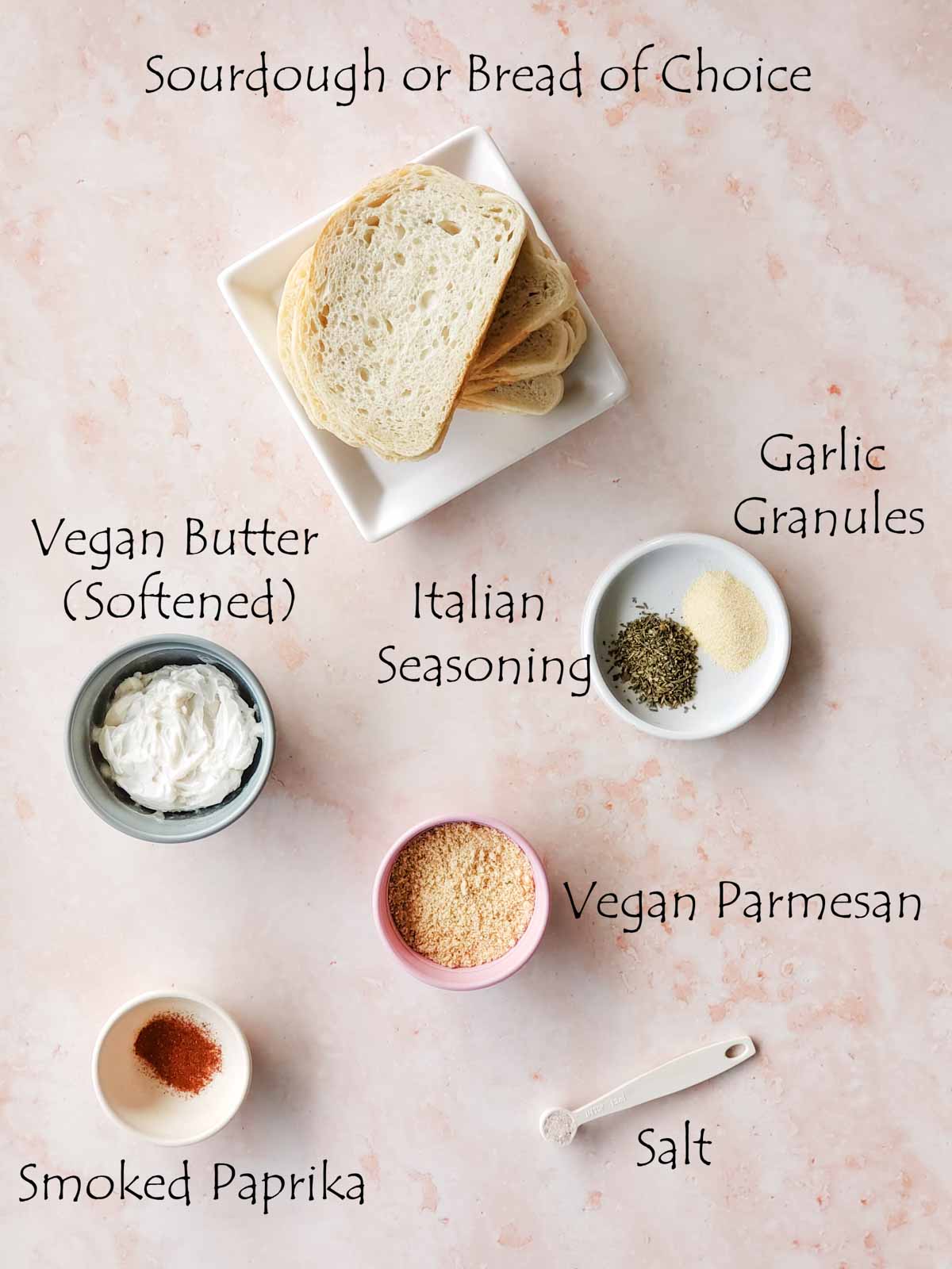 Ingredients laid out: sourdough, vegan butter, garlic granules, Italian seasoning, salt, vegan parmesan, paprika.