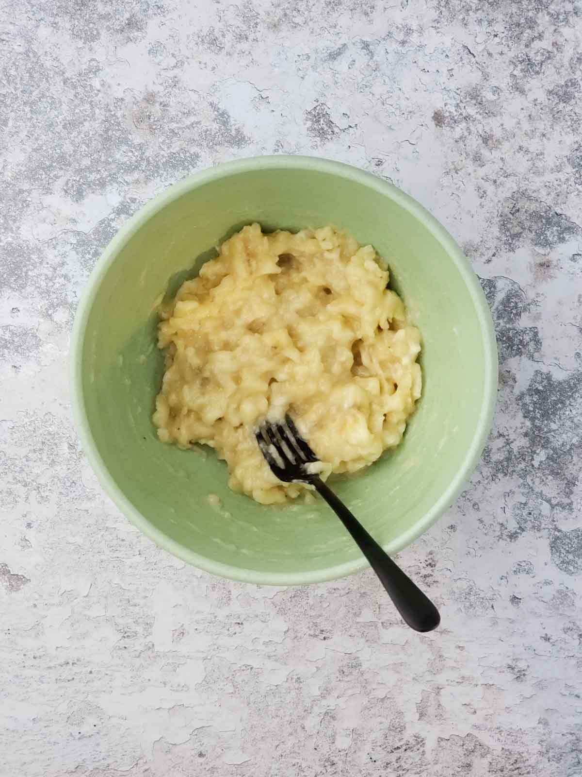 Mashed ripe bananas in a green mixing bowl with a fork.