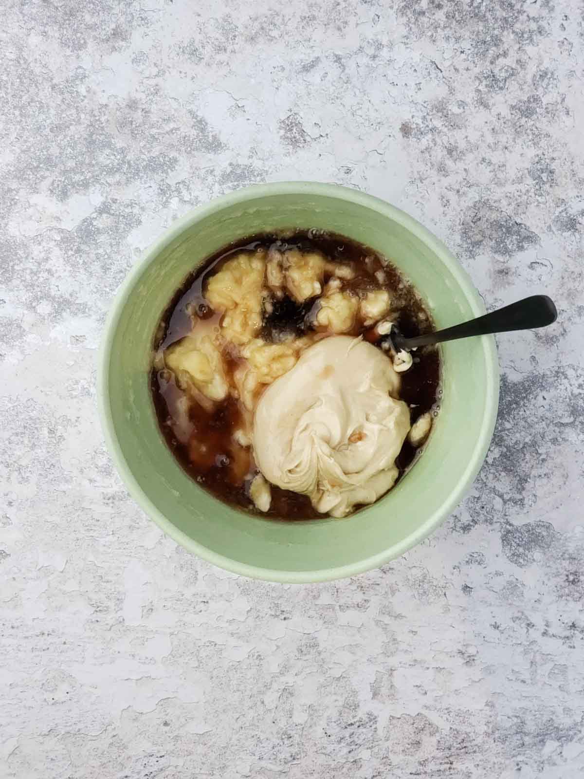 Bananas, maple syrup, vanilla, and cashew butter in a bowl before mixing for banana bread batter.