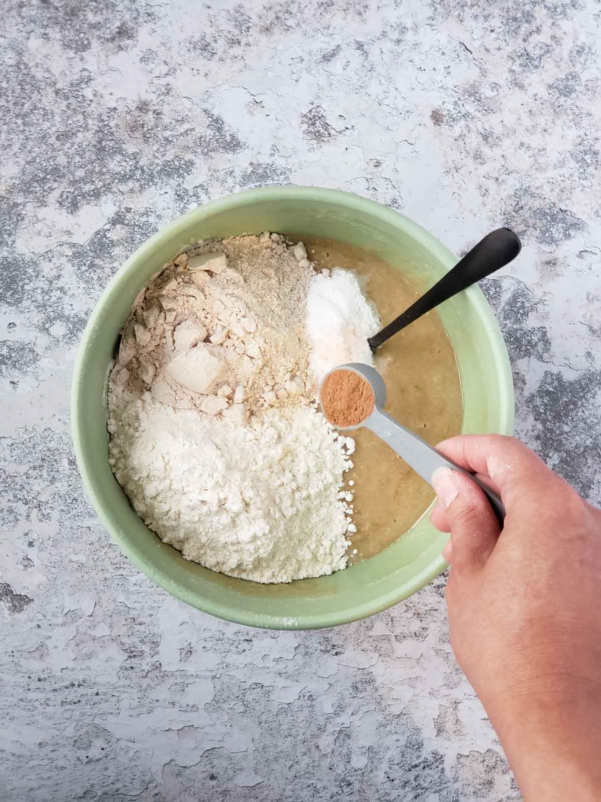 Adding flour, baking powder, and cinnamon to the wet ingredients in a mixing bowl.