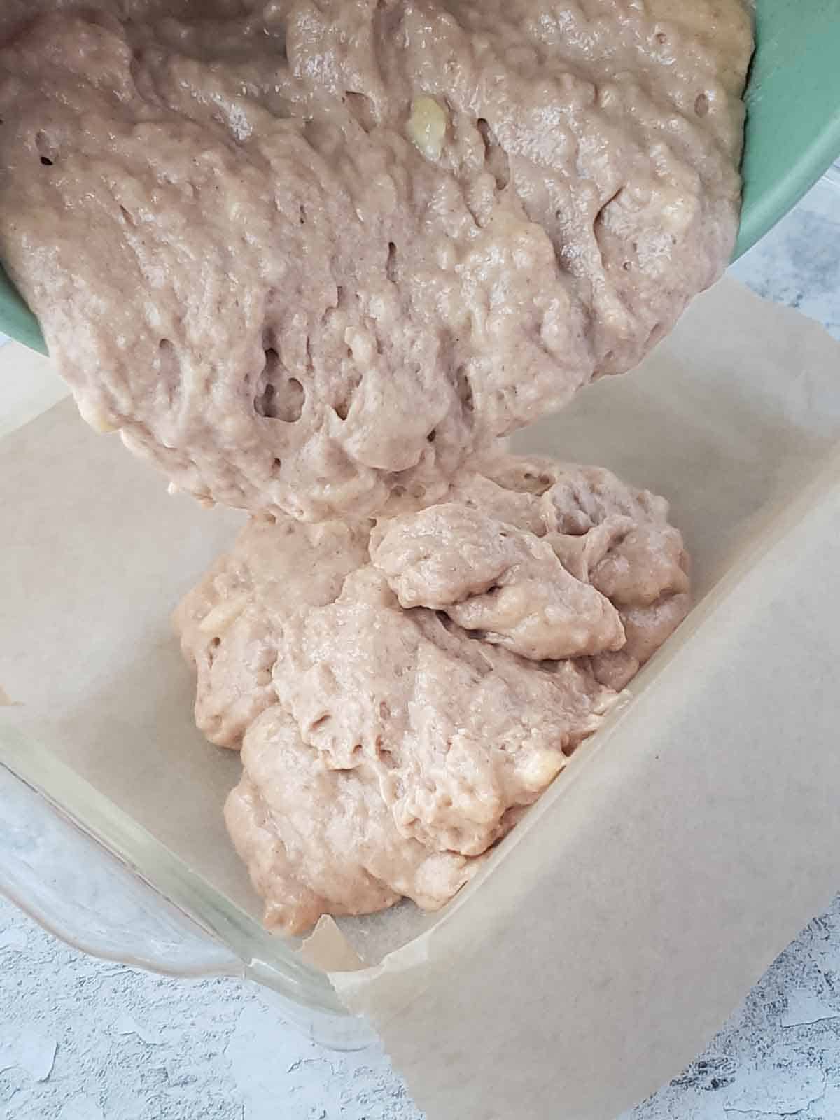 Pouring banana bread batter into a parchment-lined loaf pan.