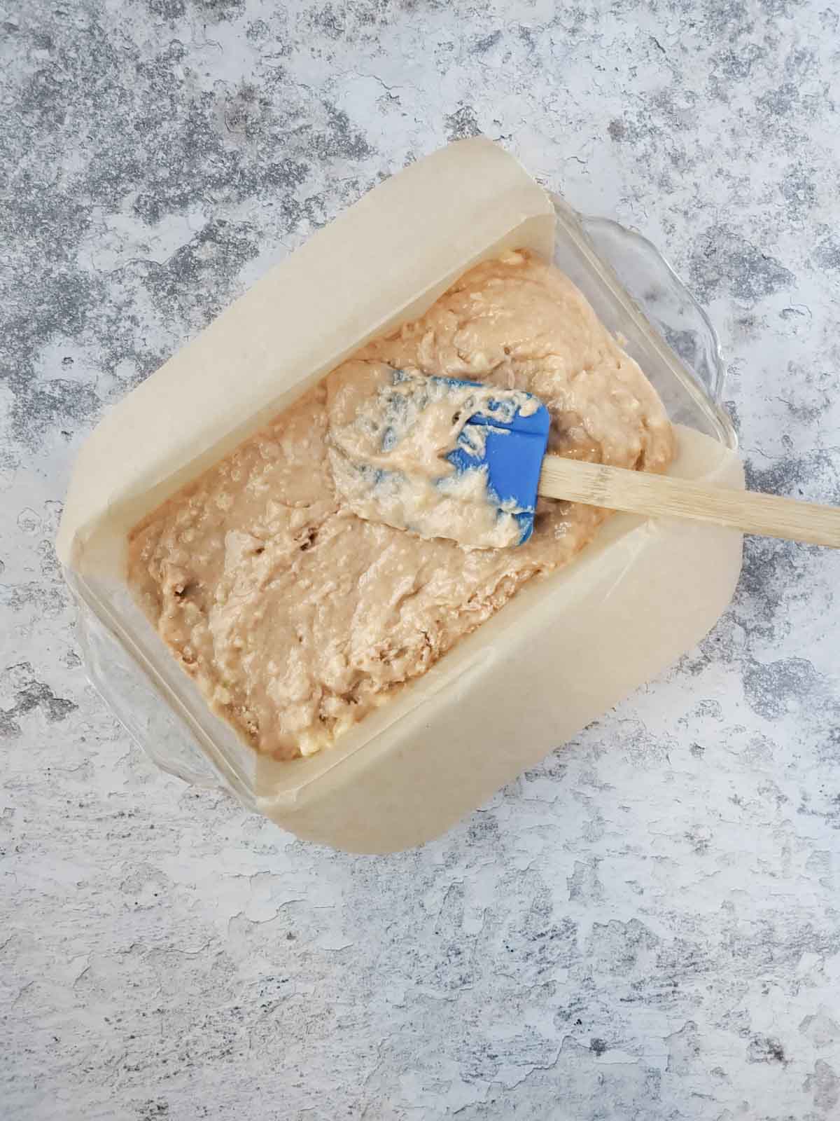 Spreading the batter evenly in a parchment-lined glass loaf pan before baking.