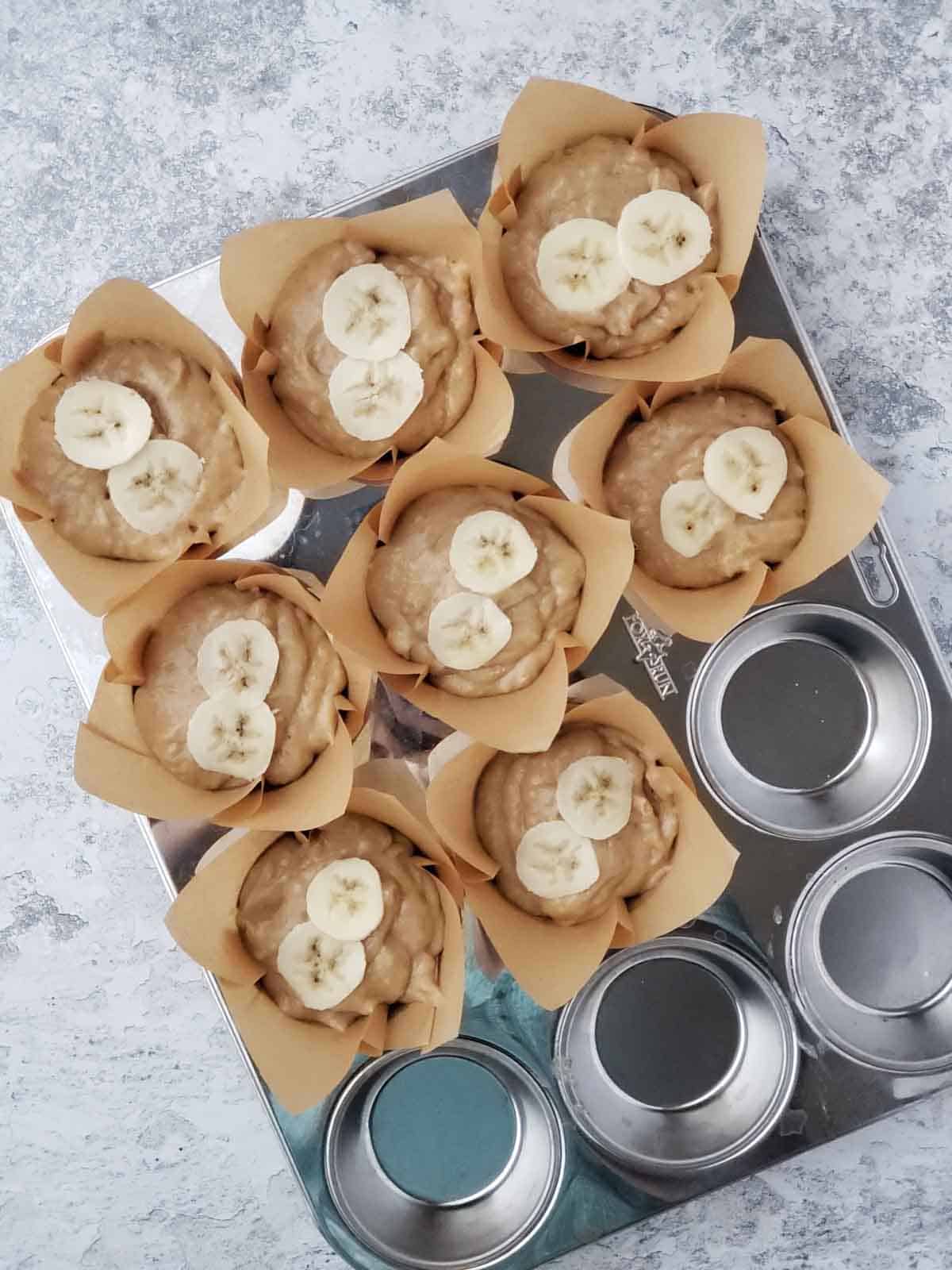 Banana bread batter divided into parchment muffin cups topped with banana slices.