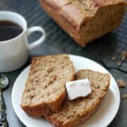 Close-up of two slices of moist vegan banana bread topped with a pat of vegan butter and a cup of coffee.