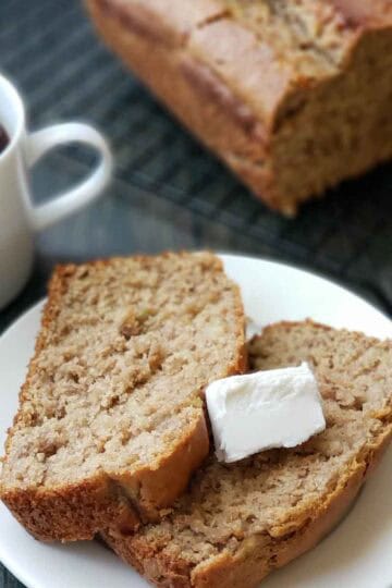 Close-up of two slices of moist vegan banana bread topped with a pat of vegan butter and a cup of coffee.