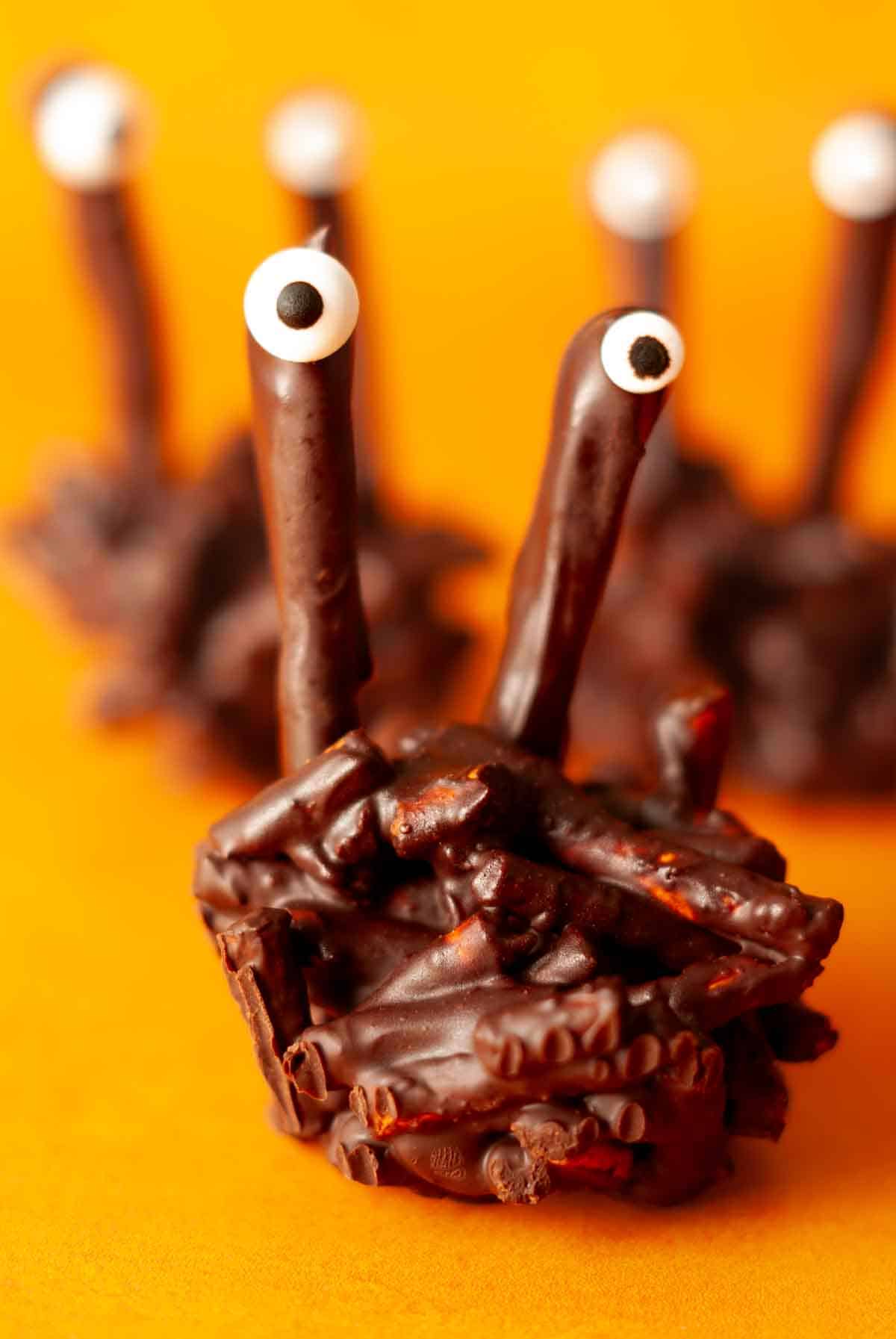 Group of chocolate pretzel monsters with candy eyes on orange background for Halloween treats.