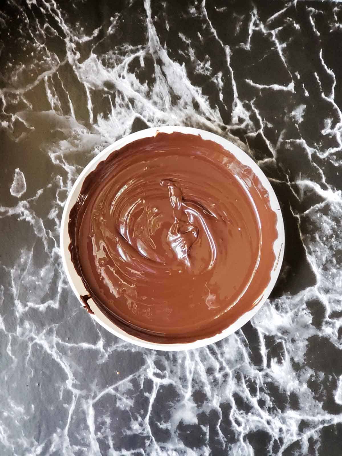 Glossy melted chocolate being stirred in a white bowl.