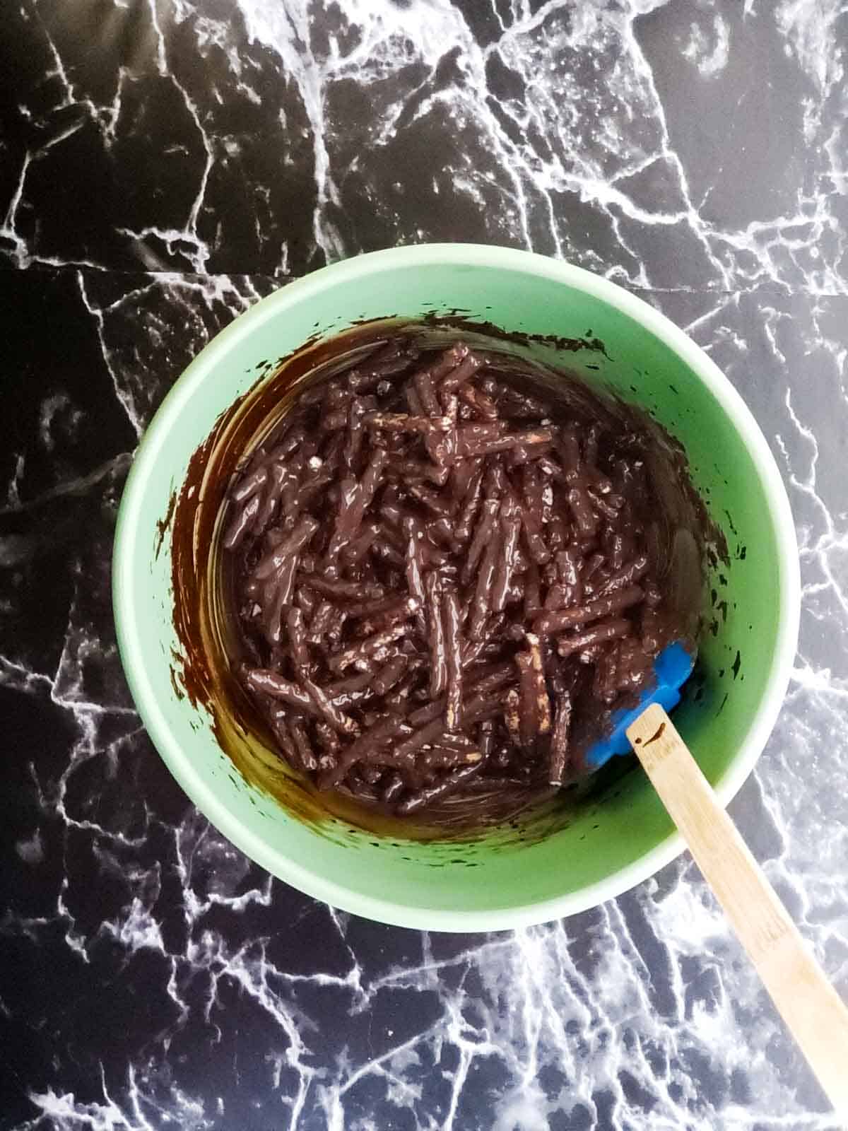 Stirring the melted chocolate in a green mixing bowl to coat the sticks.