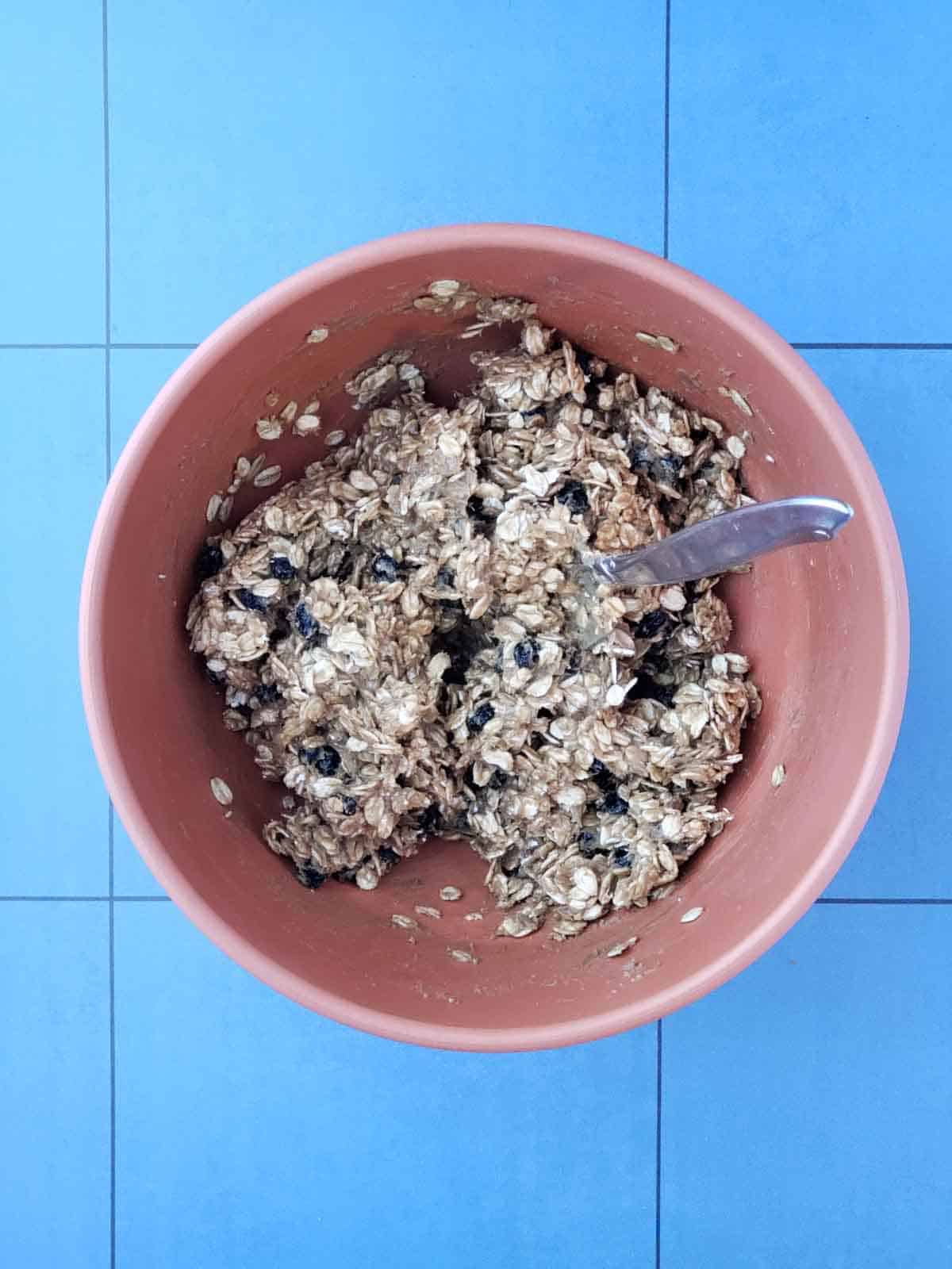 Mixing bowl filled with oats and dried blueberries coated in sunbutter mixture being stirred together.