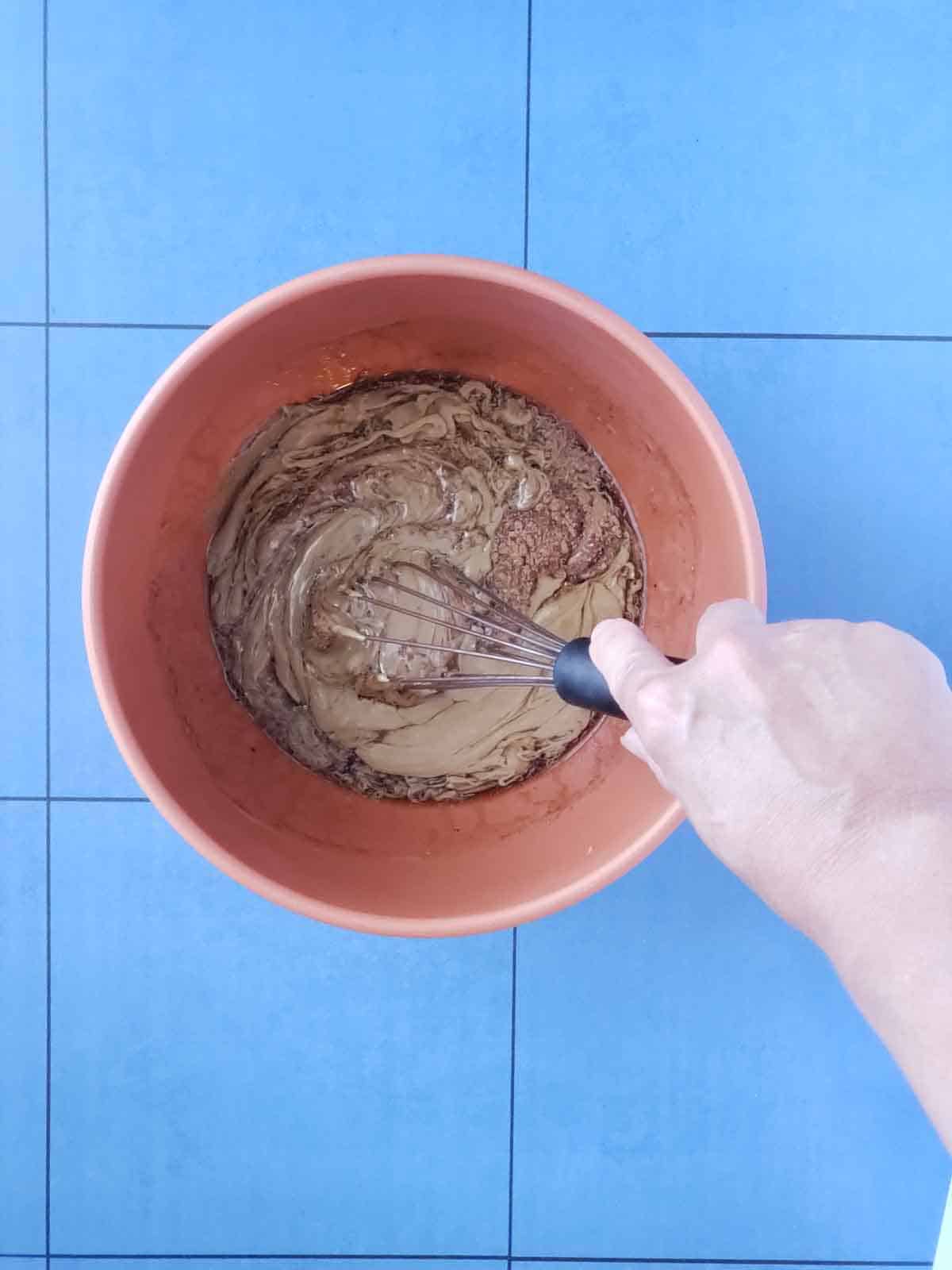 Hand whisking together sunbutter, maple syrup, and cinnamon in a mixing bowl.