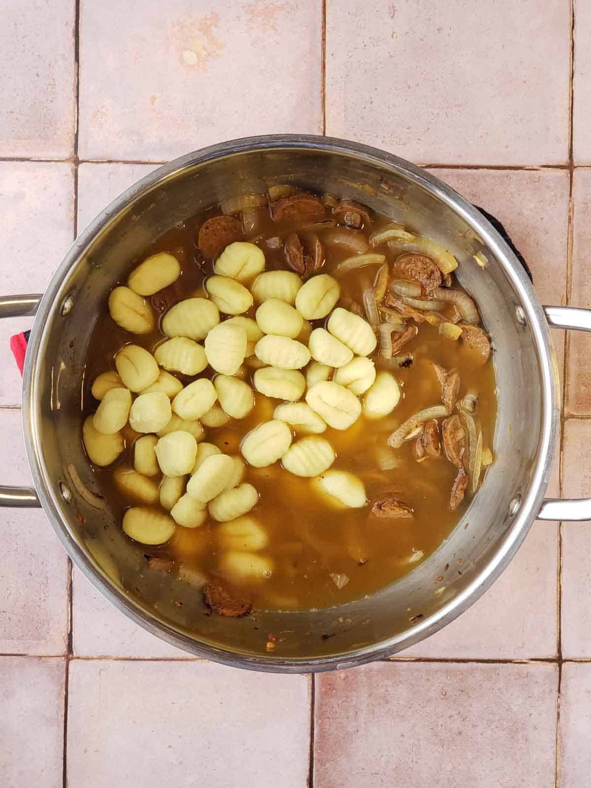 Potato gnocchi added to the pot with broth and vegan sausage mixture before simmering.