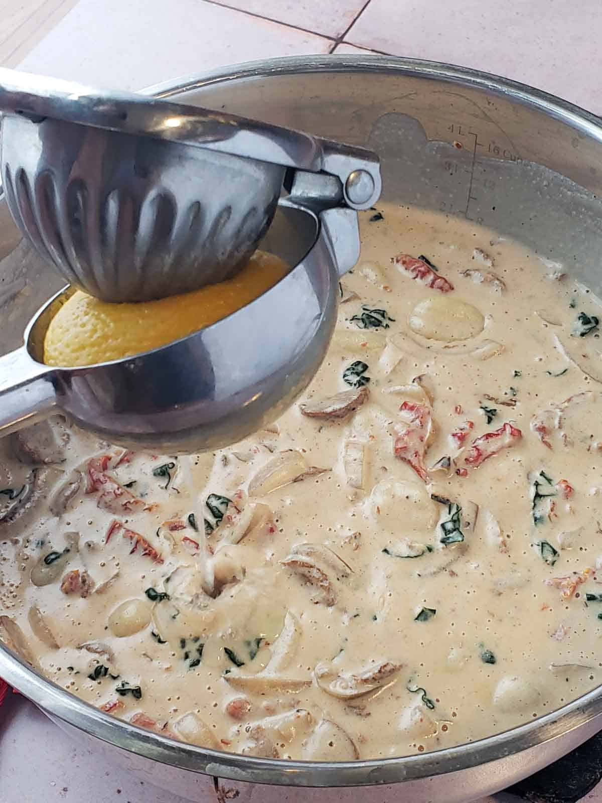 Fresh lemon being squeezed over creamy vegan Tuscan gnocchi in a large pot for a bright finishing touch.