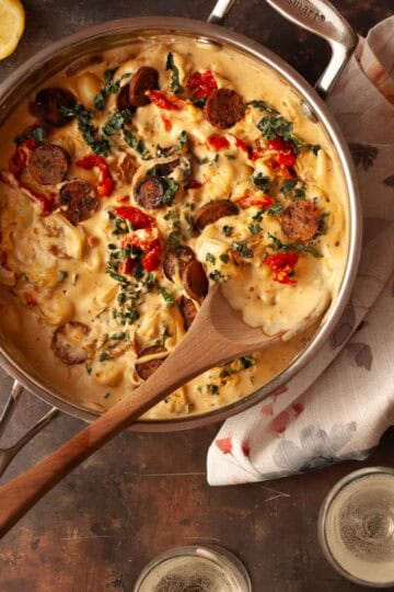 Close-up of creamy vegan Tuscan gnocchi with kale, sausage, and sun-dried tomatoes in a pan on a dark background.