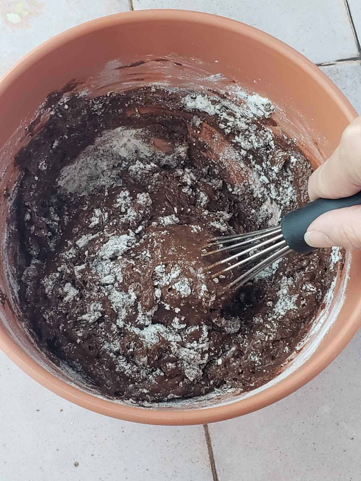 A hand mixing thick fudgy vegan cookie dough with whisk in orange bowl.