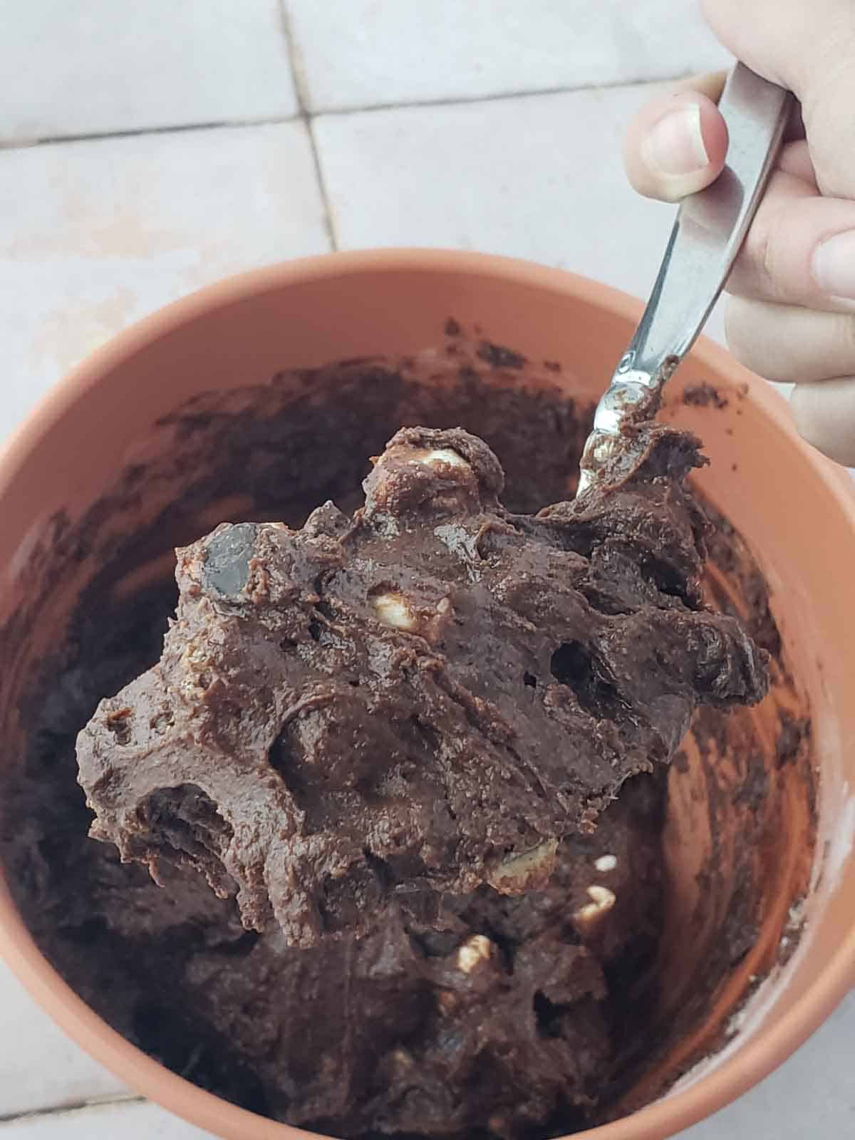 Scooping rich brownie cookie dough with marshmallows ready to bake.