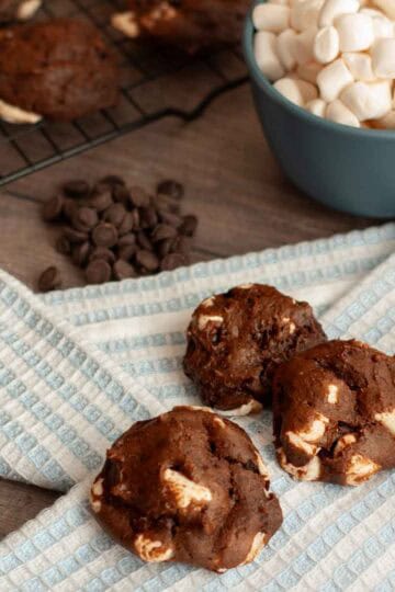 Close up of three vegan chocolate marshmallow cookies beside bowl of mini marshmallows.