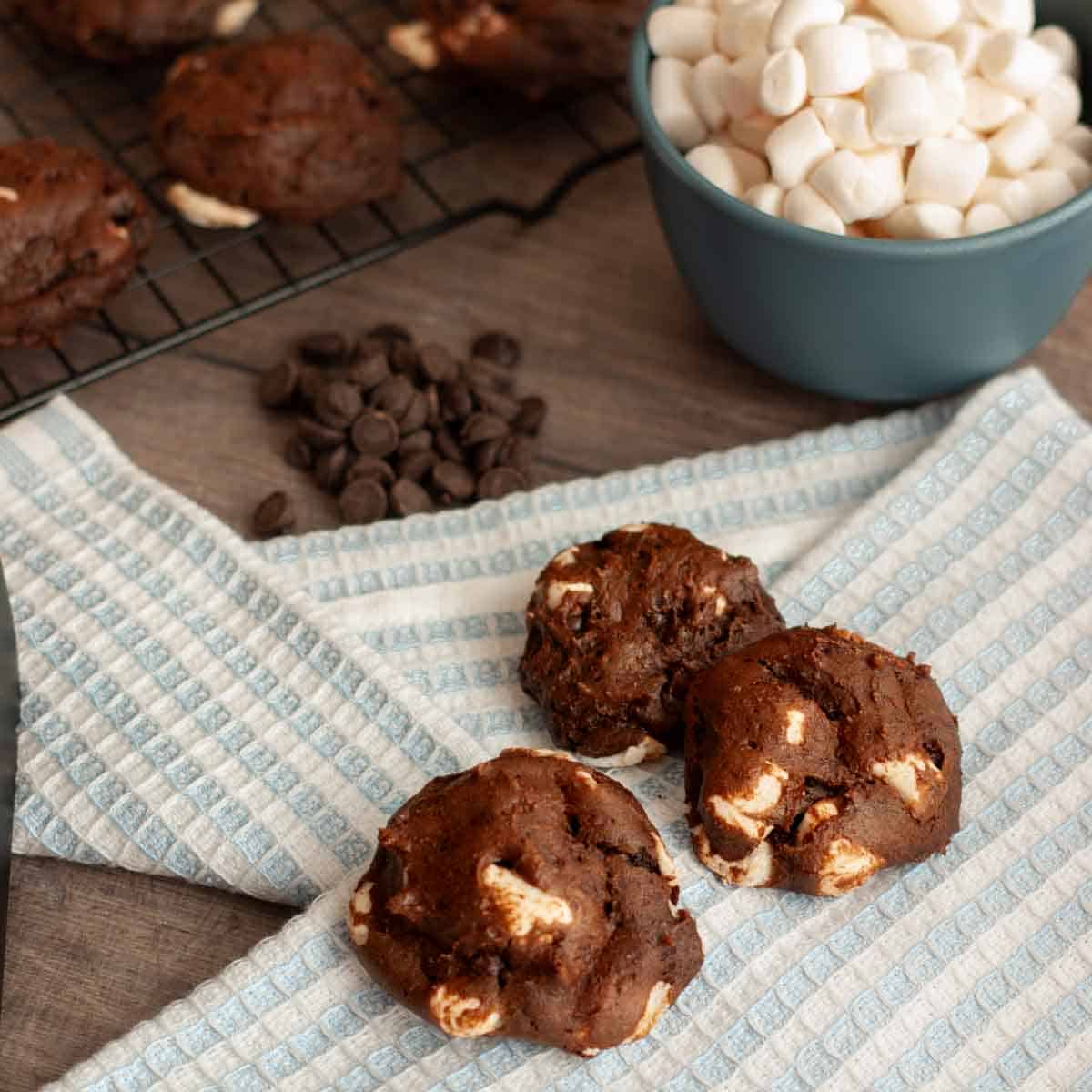 Close up of three vegan chocolate marshmallow cookies beside bowl of mini marshmallows.