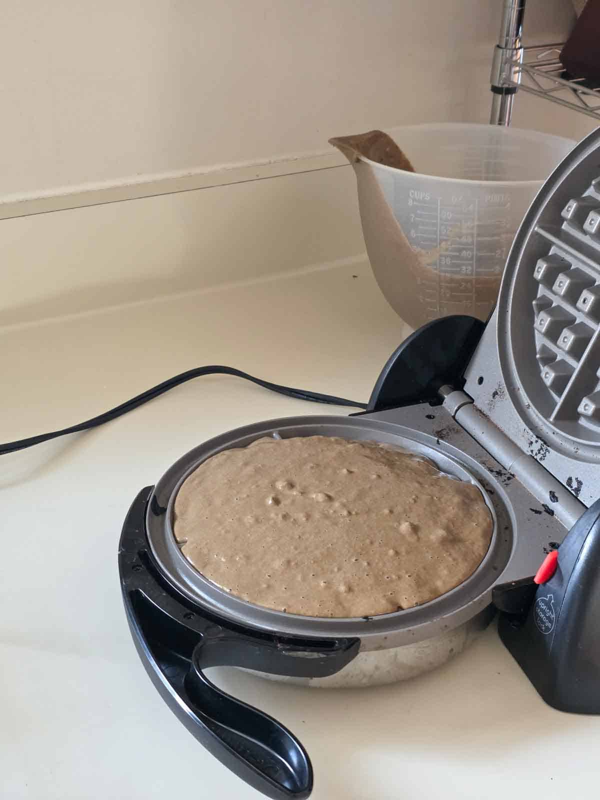 Batter poured into a Belgian waffle maker, filling the round plate and ready to cook into a fluffy chocolate waffle.
