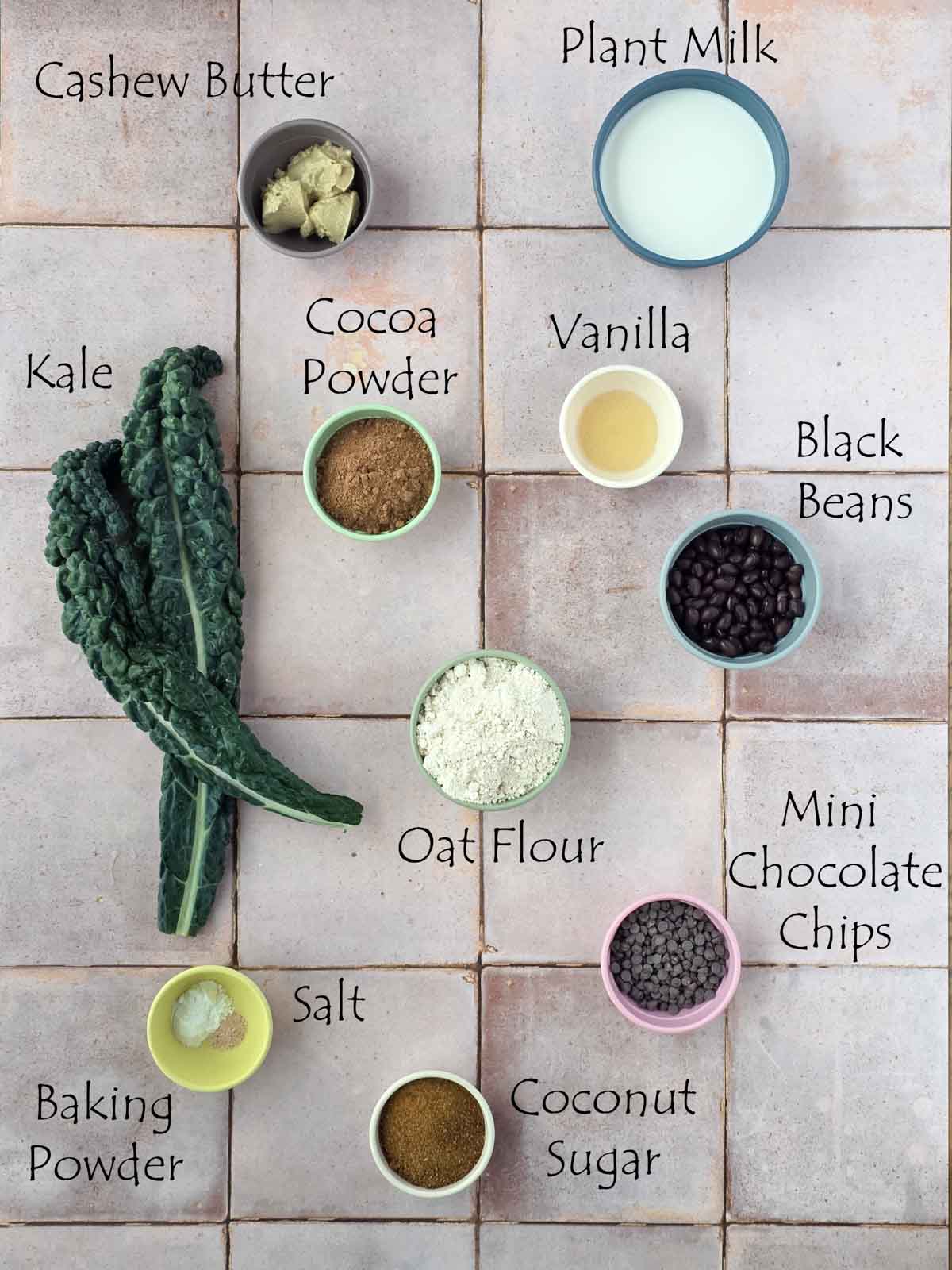 Flat lay of labeled ingredients for vegan chocolate waffles, including kale, cocoa, oat flour, beans, and cashew butter.