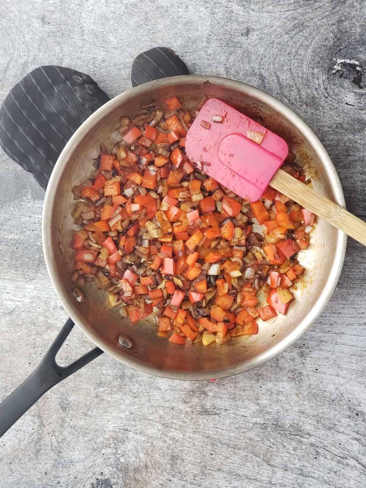 Softened peppers and onions in a pan after sautéing, adding flavor and color to the enchilada casserole base.