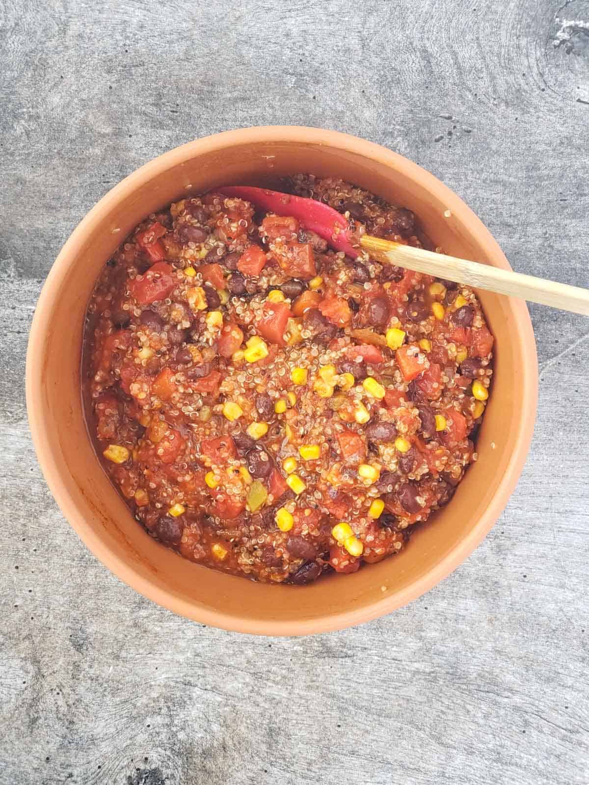 Recipe ingredients stirred together in a large bowl, showing colorful quinoa, corn, beans, and Rotel tomatoes.