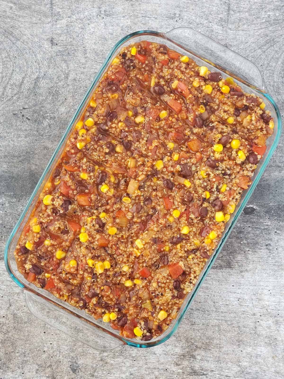 Unbaked vegan enchilada bake spread evenly in a glass casserole dish, ready for the oven.