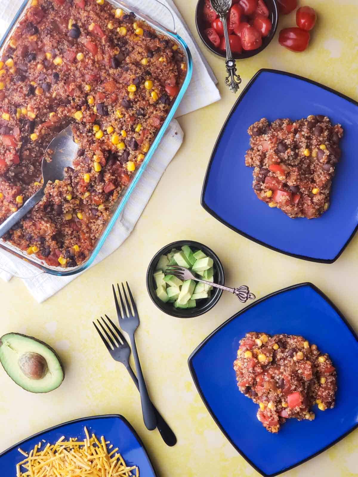 Baked vegan enchilada casserole served with diced avocado and tomatoes, a hearty plant-based meal ready to enjoy.