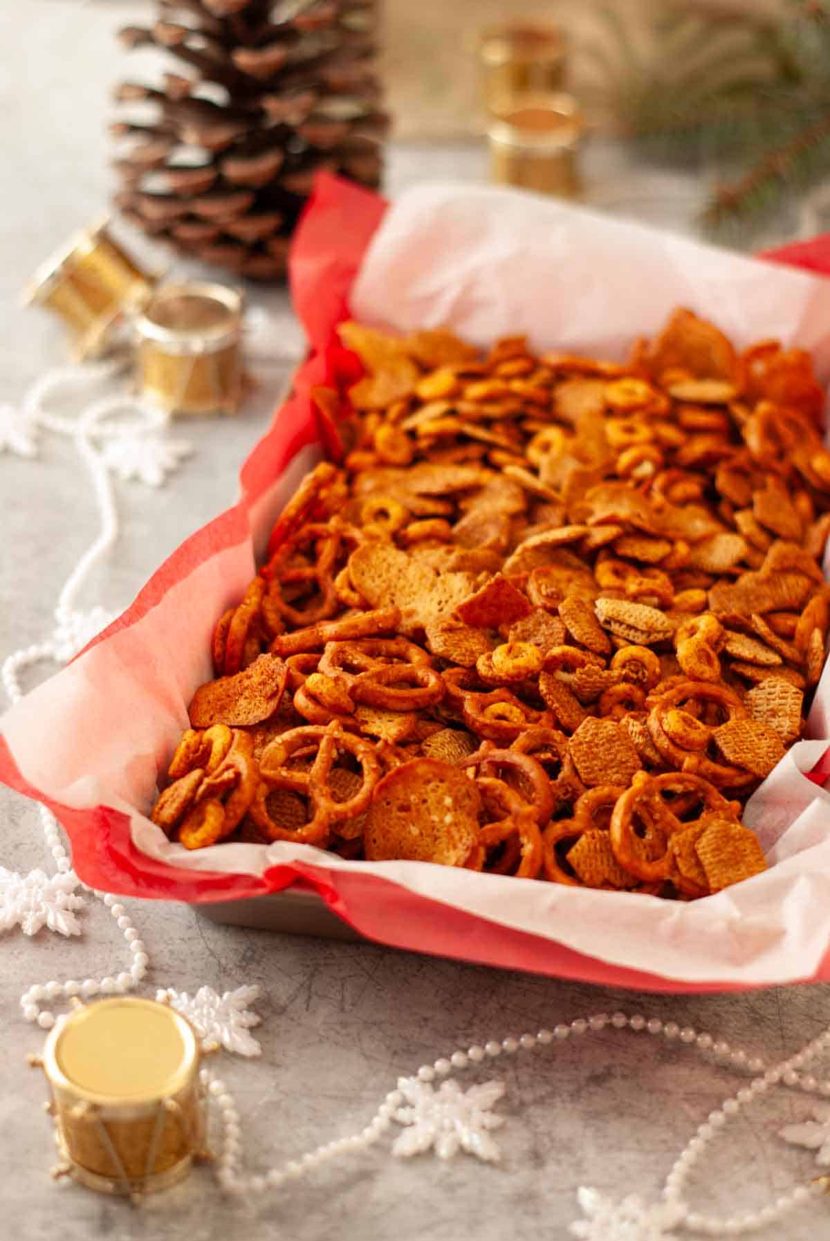 Festive bowl of crunchy homemade Vegan Chex Mix with pretzels, cereal, and bagel chips lined in red and white tissue paper.
