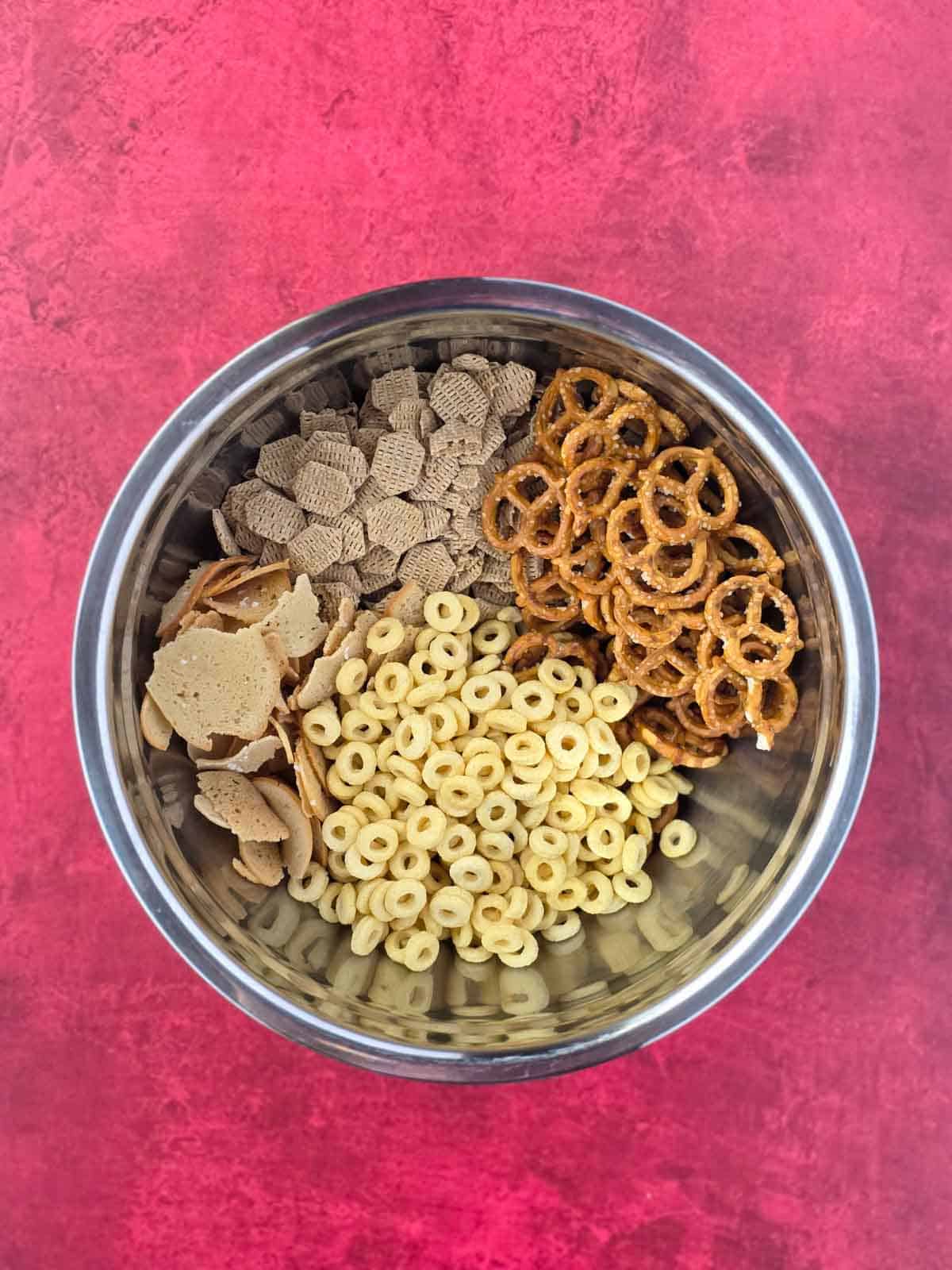 Big stainless bowl filled with cereals, pretzels, and bagel chips before adding seasoning.