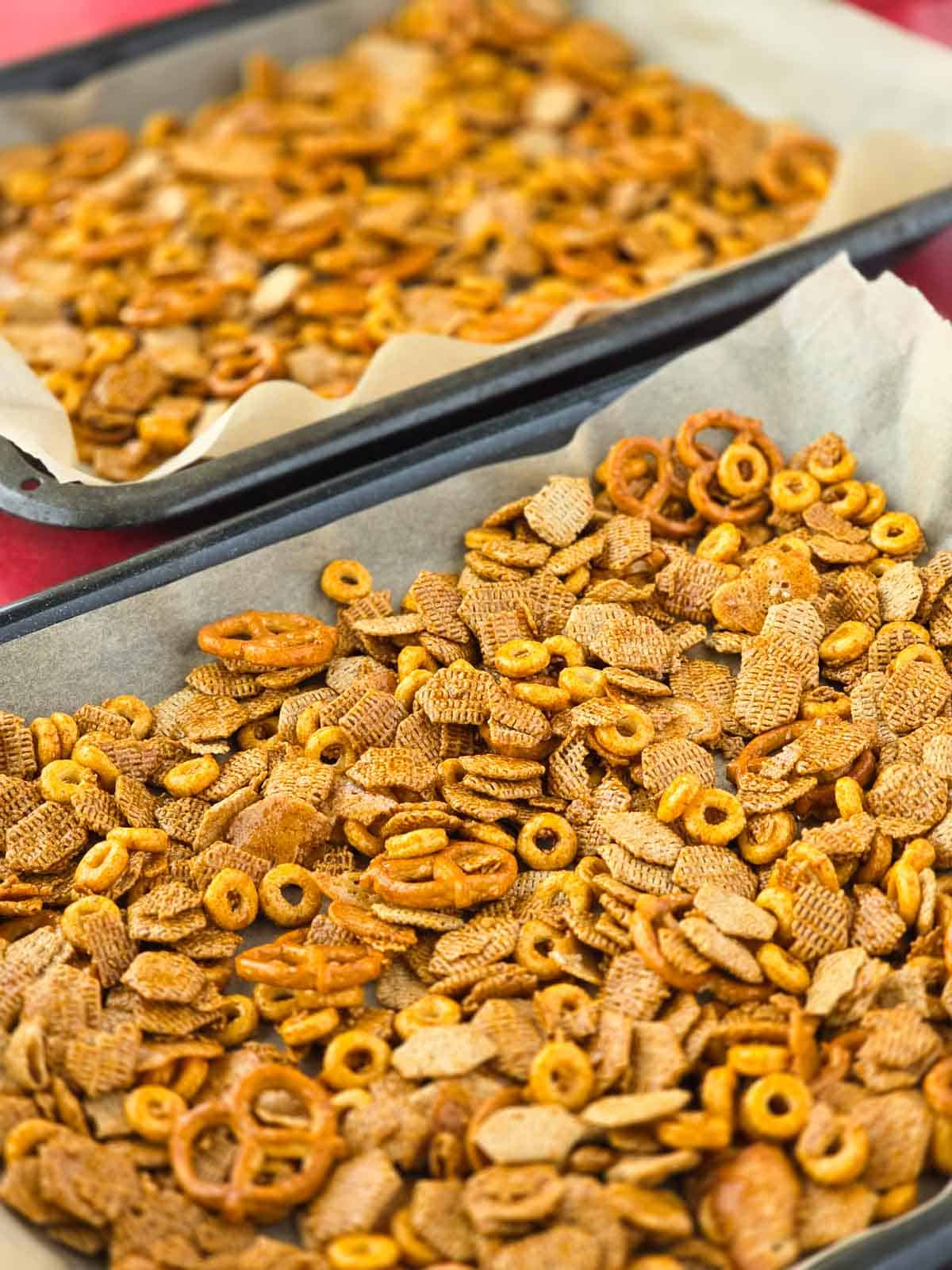 Golden, seasoned cereal and pretzels spread across sheet pans before baking.