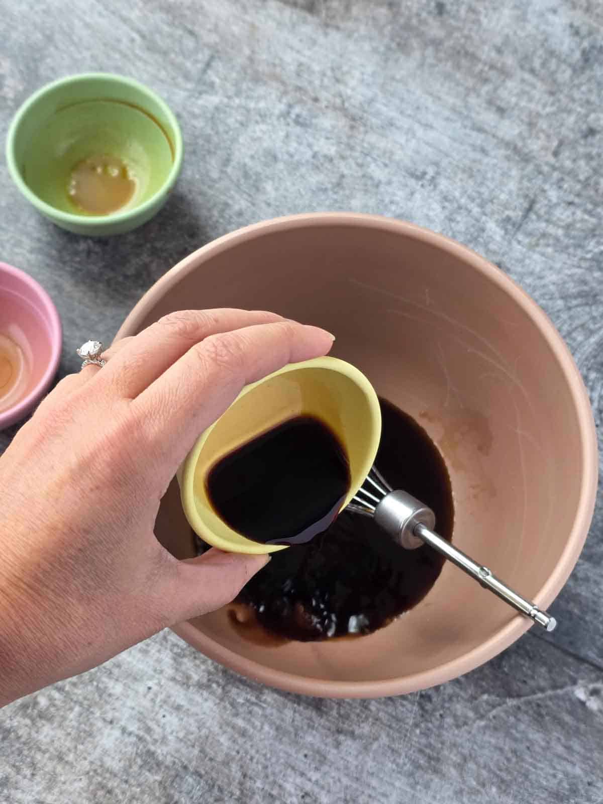 Soy sauce, vinegar, and maple syrup poured into a mixing bowl to make marinade.