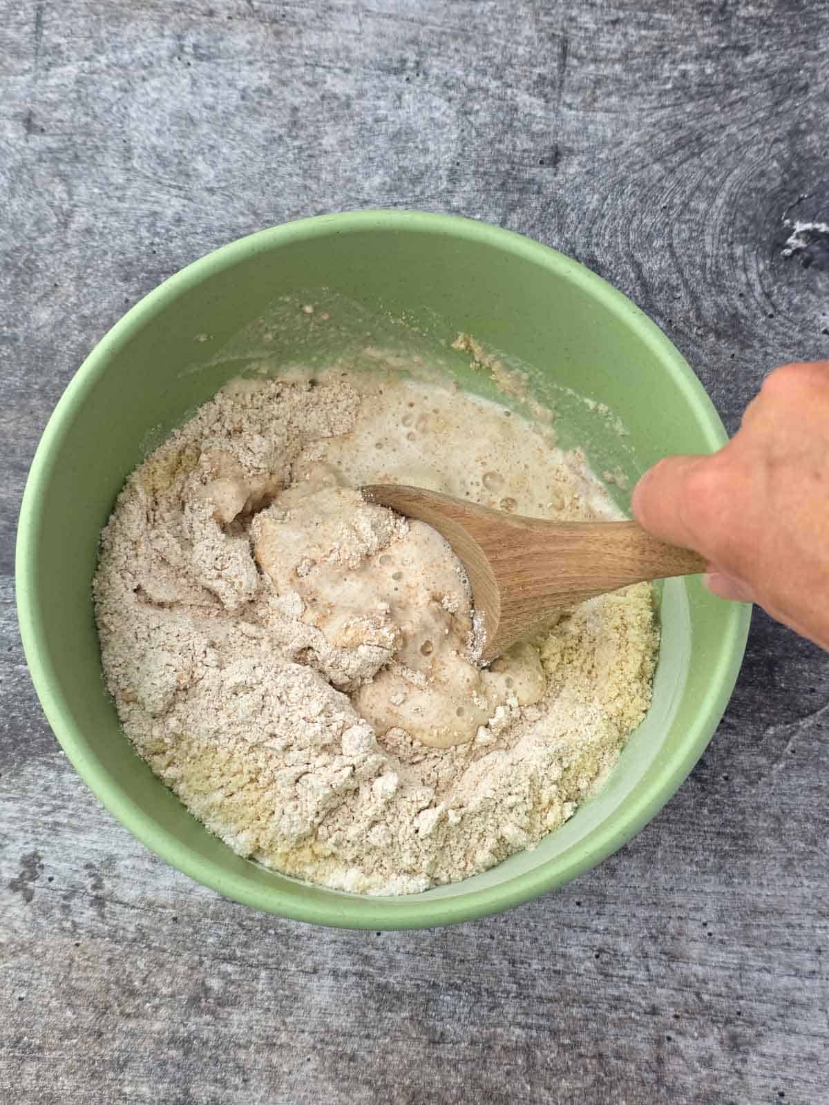 Partially mixed biscuit dough being stirred with a wooden spoon in a green bowl.