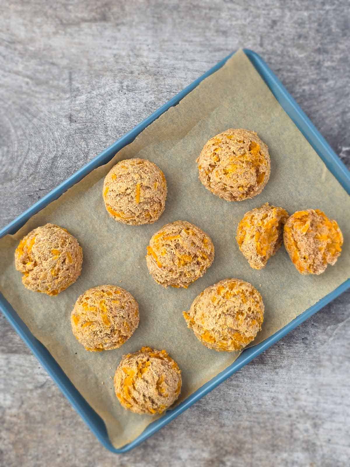 Freshly baked vegan garlic cheese biscuits on a parchment-lined baking sheet cooling after baking.
