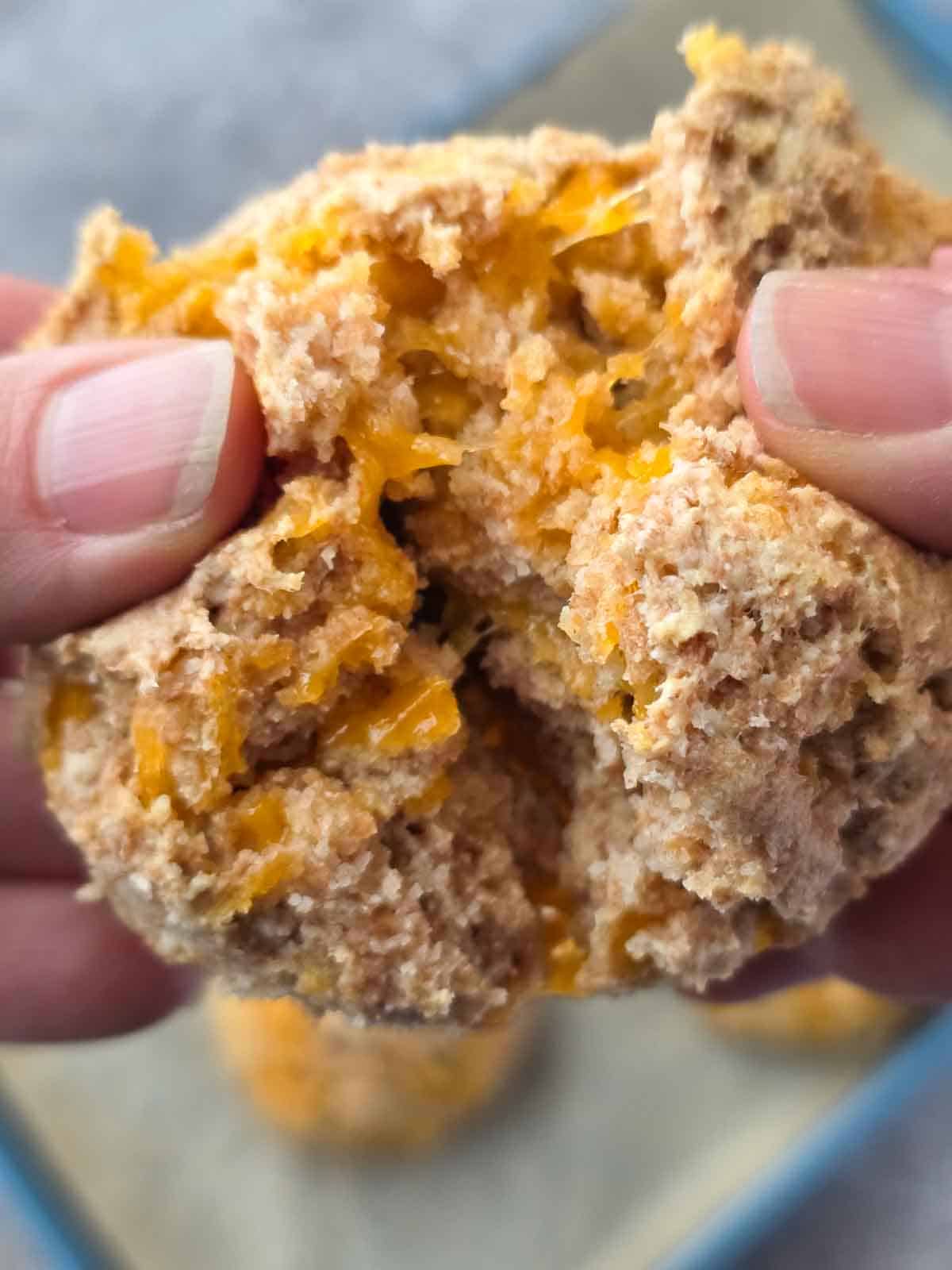 Close-up of hands pulling apart a warm biscuit to show the soft interior and melted cheese.