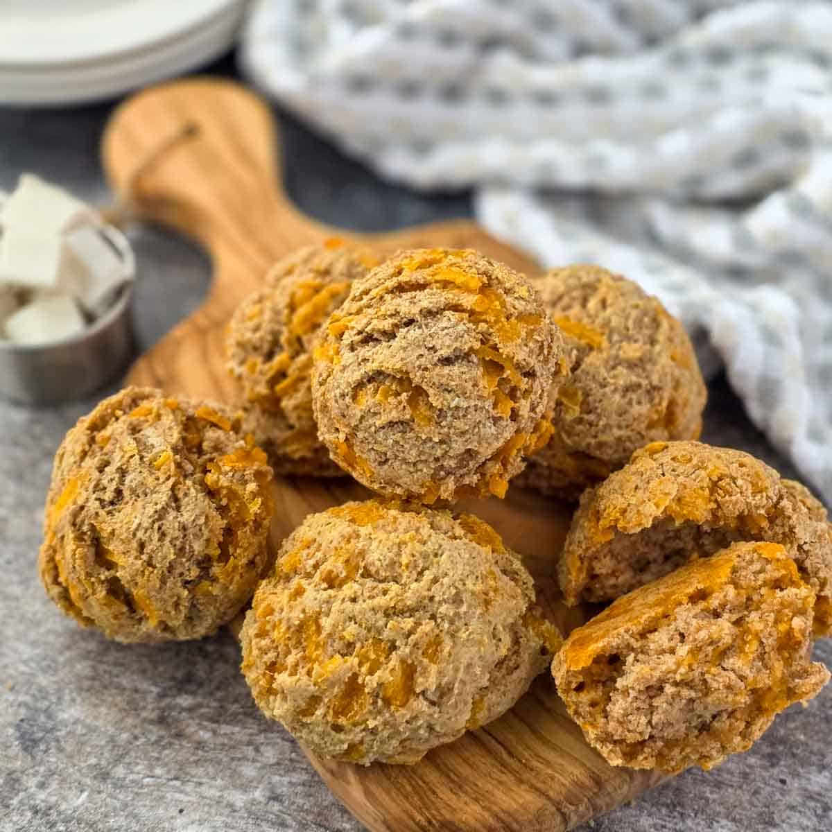 Overhead view of several baked vegan garlic cheese biscuits arranged on a wooden board with a bowl of vegan butter nearby.