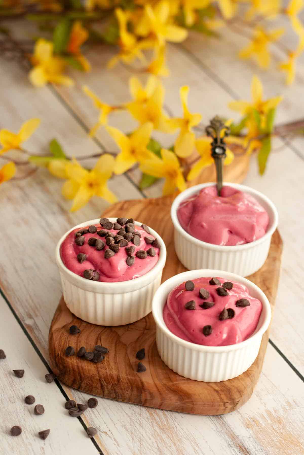 Three ramekins of raspberry pudding arranged on a wooden board.